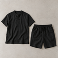 one black men's two-piece set consisting of a collarless short-sleeve henley with a three-button placket and matching drawstring shorts arranged side by side, both fully visible
